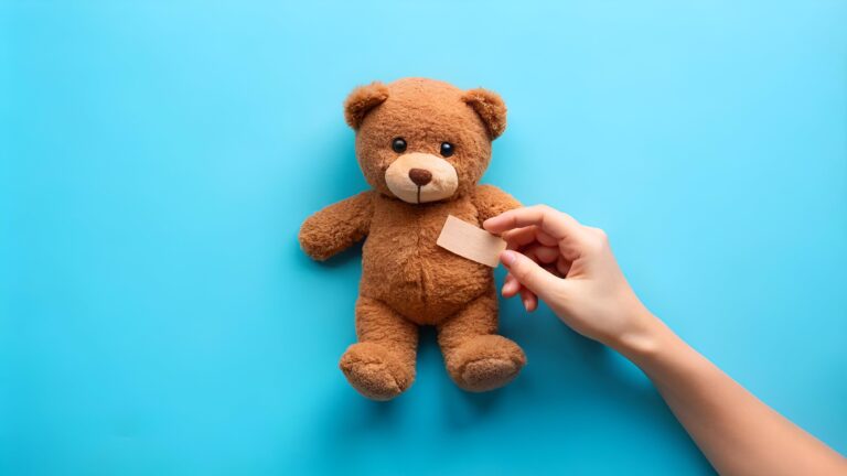 female hand holds a brown teddy bear and glues a medical adhesive plaster on a blue background, tram treatment